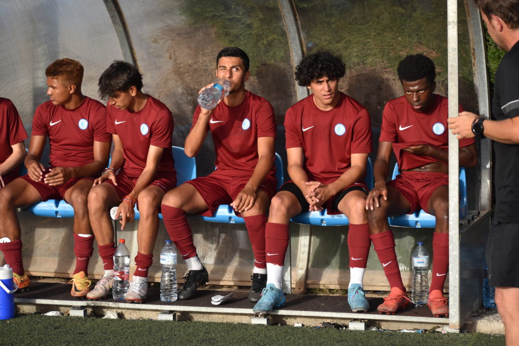 College soccer players listening to coach on the bench during a game.